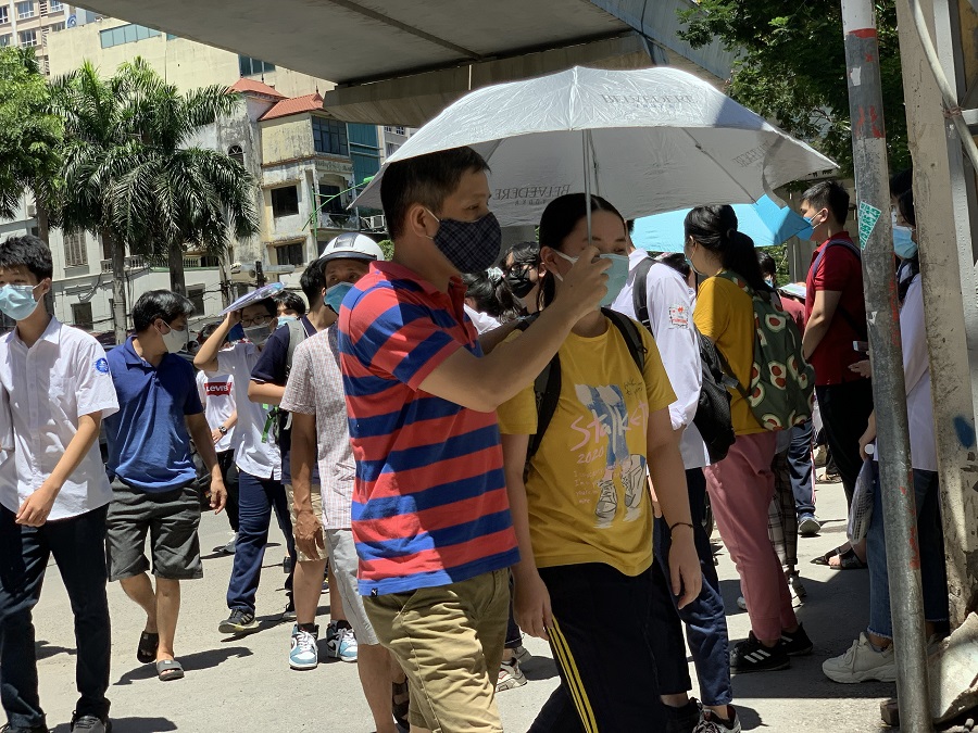A group of people walking down a sidewalk under an umbrellaDescription automatically generated with medium confidence